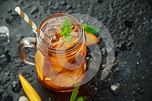 Peach Ice tea with mint in glass jar, on rustic black background. summer fruit cold drinks