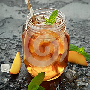 Peach Ice tea with mint in glass jar, on rustic black background. summer fruit cold drinks