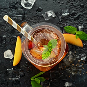 Peach Ice tea with mint in glass jar, on rustic black background. summer fruit cold drinks