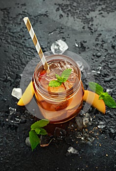 Peach Ice tea with mint in glass jar, on rustic black background. summer fruit cold drinks