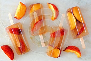 Peach iced tea popsicles with fruit slices on white marble