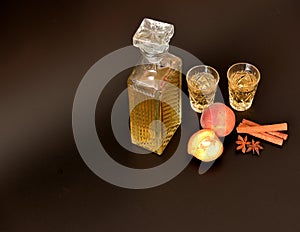 Peach liqueur with spices on a black background, a crystal decanter and two glasses of strong homemade alcohol, anise and cinnamon