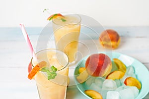 Peach refreshing juice cocktail in a glass with ice and pieces of fruit and mint in the summer. top view on a light background