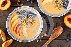 Peach smoothie bowls with blueberries and granola, top view table scene over dark wood