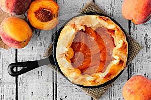 Peach tart in cast iron skillet, overhead on white wood