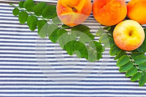 Peaches, apple and green leaves on striped textile background. Frame, top view. Free space for your text or product
