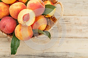 Peaches in a basket on a wooden background with a slice of sliced juicy peach with a stone.