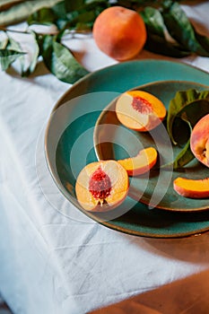 Peaches fruit Still life in minimalistic rustic style. Peaches with leaves on color green plate on table with white tablecloth.