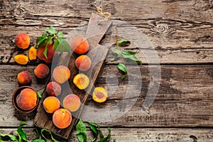Peaches with leaves on dark wooden board with peach in halves. Composition with ripe juicy peaches Harvest for food. Fresh organic