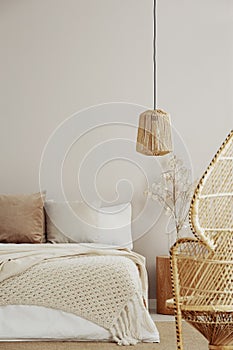 Peacock chair, wicker chandelier and cozy bed, copy space on empty wall