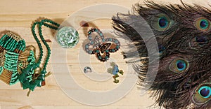 Peacock Feathers With Green Beads and Green and Copper Butterfly Broach on Wooden Background