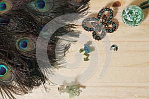 Peacock Feathers With Green Beads and Green and Copper Butterfly Broach on Wooden Background