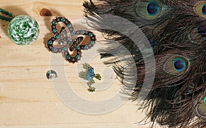 Peacock Feathers With Green Beads and Green and Copper Butterfly Broach on Wooden Background