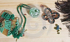 Peacock Feathers With Green Beads and Green and Copper Butterfly Broach on Wooden Background