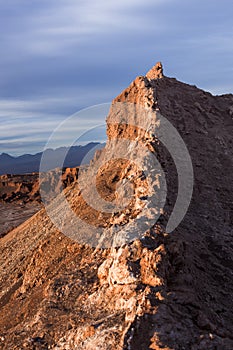 A peak in moon valley in the atacama desert (driest desert on earth) is bathed in the light of the setting sun in front of a storm