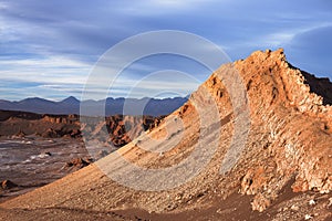 A peak in moon valley in the atacama desert (driest desert on earth) is bathed in the light of the setting sun in front of a storm