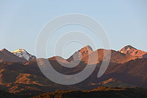 The peaks of the mountains of the Trans-Ili Alatau under the blue morning sky over the spacious slopes during sunrise.