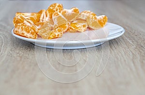 Pealed mandarin peaces on white plate, wooden desk surface