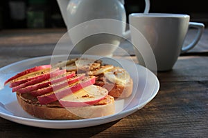 Peanut butter banana apple cinnamon sandwiches and cup of tea on table. Slices of bread with peanut paste and fruits