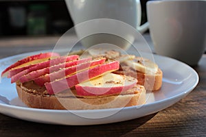 Peanut butter banana apple cinnamon sandwiches and cup of tea on table. Slices of bread with peanut paste and fruits