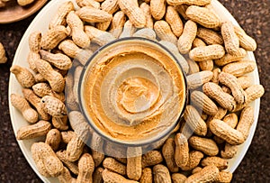 Peanut butter in a glass bowl over raw peanuts background. Creamy smooth peanut butter in glass bowl