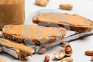 Peanut butter in a glass jar, peanuts, kitchen knife and peanut butter sandwiches on white background. Vegan food