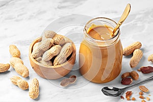 Peanut butter in glass jar and peanuts in wooden bowl on marble table