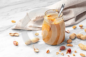 Peanut butter in glass jar with spoon on white marble table