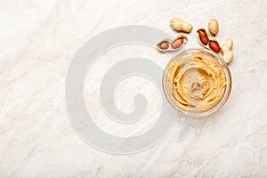 Peanut butter in a glass plate with peanuts in shell and peeled peanuts. Creamy peanut paste flat lay with place for text on white