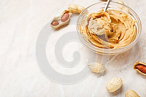 Peanut butter in glass plate with peanuts in shell, peeled peanuts, spoon with peanut butter. Creamy peanut paste flat lay with