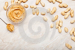 Peanut butter in glass plate with peanuts in shell, spoon with peanut butter. Creamy peanut paste flat lay with place for text on