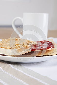 Peanut butter and jam on slices of bread with cup of coffee