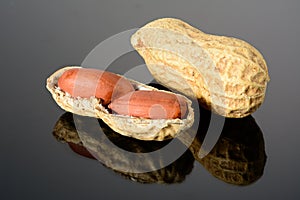 Peanut on glossy black surface with reflection. Whole peanut and open shell with two kernels macro close-up, high resolution full