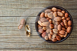 Peanut in nutshell in brown bowl on wooden background. Composition of peanuts