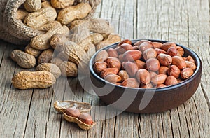 Peanut in nutshell in burlap sack or sackcloth and bowl on wooden background. Composition of peanuts