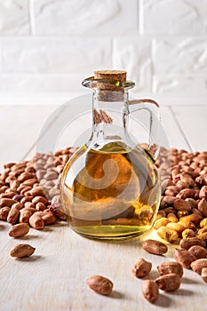 Peanut oil in a glass jug and raw peanuts on a white wooden table. Monounsaturated cooking oil made of Arachis hypogaea. Groundnut photo