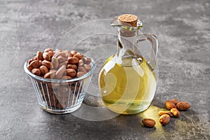 Peanut oil in a glass jug and raw peeled groundnut in a glass bowl over gray background. Arachis hypogaea as edible seeds and oil