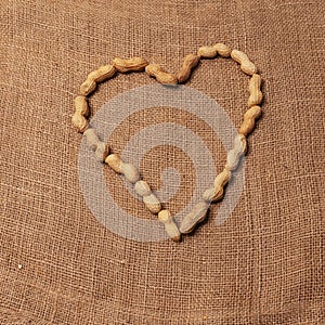 Peanuts . arranged to form a heart. Rustic background of raw yuta canvas. Delicious food. photo