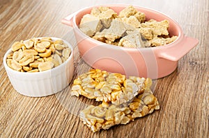 Peanuts in bowl, pieces of peanut halva in oval bowl, pieces of kozinak on wooden table