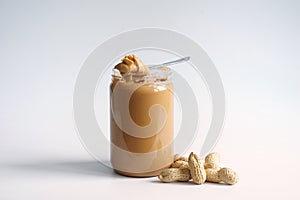 Peanuts butter in a clear glass bottle and pile of peanuts placed on white background.