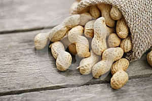 Peanuts in a miniature burlap bag on old, gray wooden surface