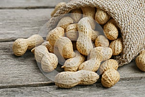 Peanuts in a miniature burlap bag on old, gray wooden surface