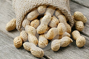 Peanuts in a miniature burlap bag on old, gray wooden surface