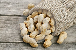 Peanuts in a miniature burlap bag on old, gray wooden surface