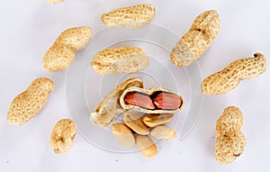 Peanuts scattered on a white background. One was opened to reveal a red seed inside