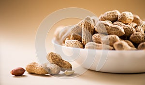 Peanuts. Unshelled nuts in a bowl close up. Roasted pile of peanuts in shell over beige background