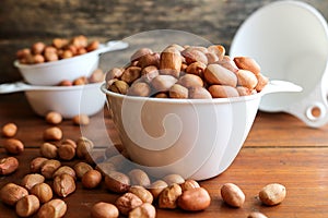 Peanuts in white measuring cup on wooden background.