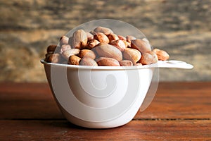 Peanuts in white measuring cup on wooden background.