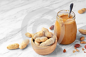 Peanuts in wooden bowl and peanut butter in glass jar on marble table