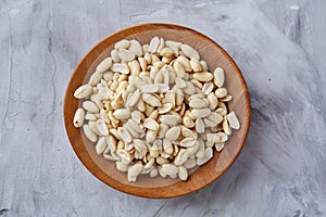 Peanuts in wooden plate over white textured background, top view, close-up.